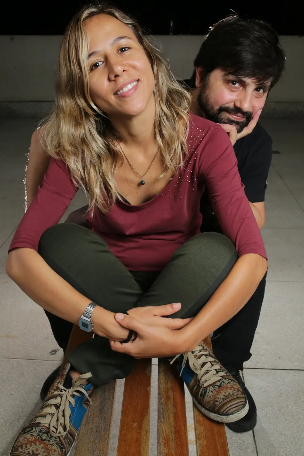Mariane Guerra e Sandro Vales sentados em um banco, sorrindo